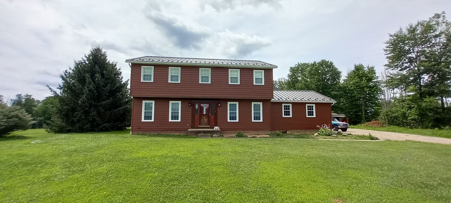 A large red brick house is sitting in the middle of a lush green field.