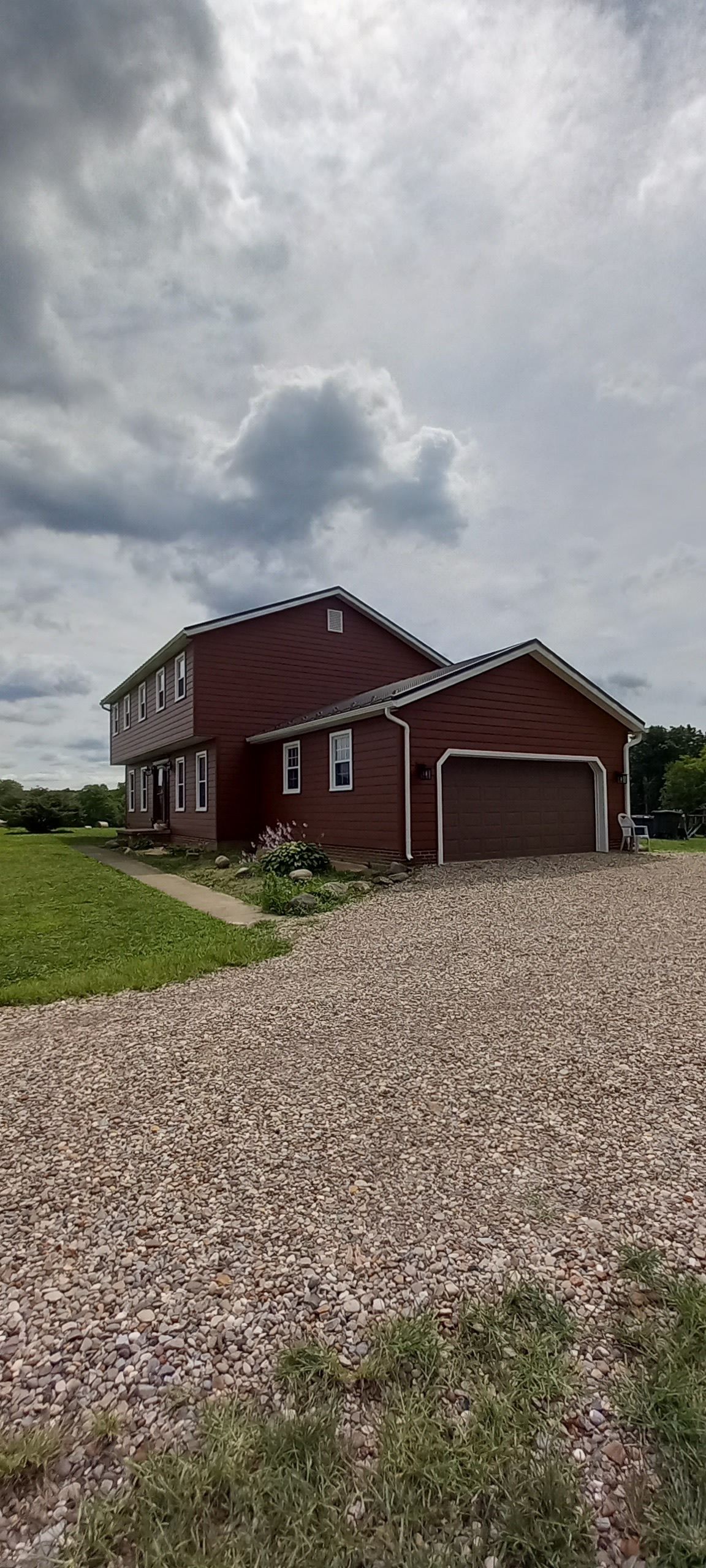 A large red house with a garage and a gravel driveway in front of it.