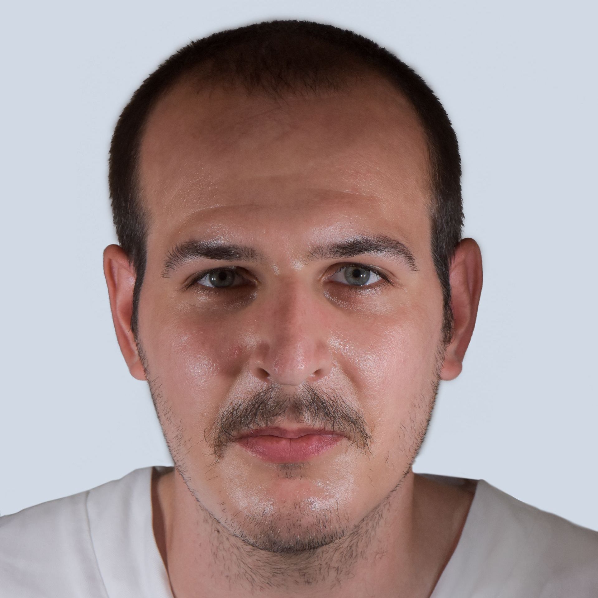 Un uomo con i capelli castani e i baffi guarda direttamente la telecamera su uno sfondo azzurro. Indossa una camicia bianca.