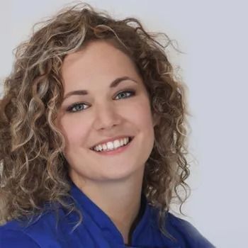 Una donna con i capelli biondi e ricci sorride, indossando una maglietta blu.