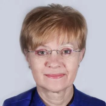 Donna con capelli biondi corti, occhiali, indossa una maglietta blu e sorride.