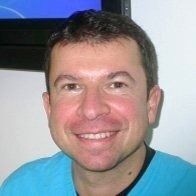 Uomo sorridente con i capelli corti e scuri, che indossa una camicia blu, in una stanza ben illuminata.