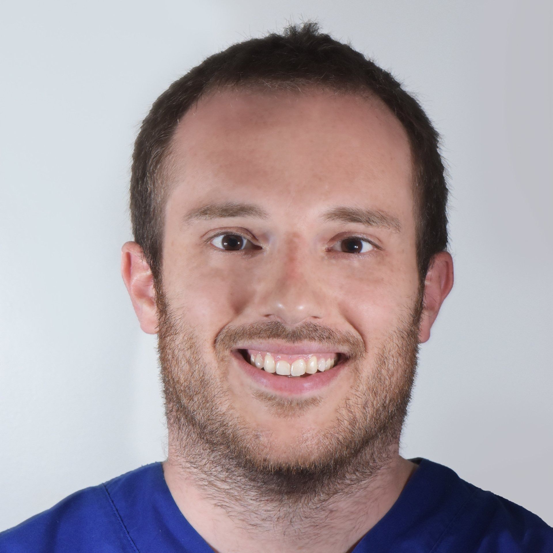 Un uomo sorridente con i capelli castani corti e la barba che indossa una camicia blu, su uno sfondo chiaro.