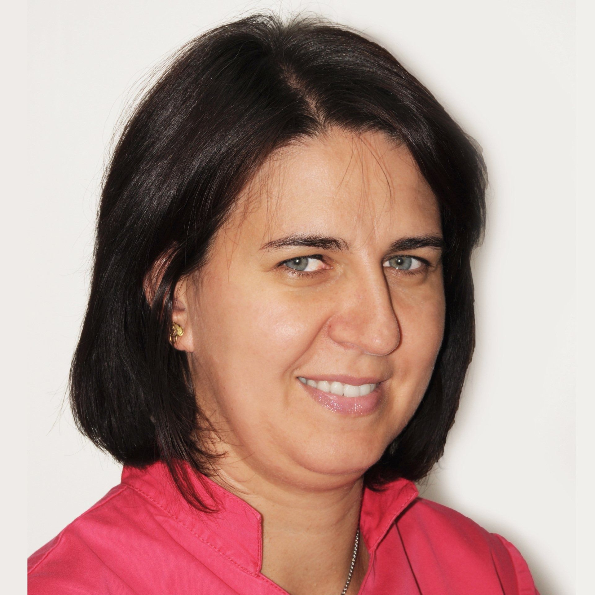 Donna sorridente con capelli scuri e pelle chiara, indossa una maglietta rosa e una collana.