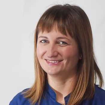 Donna con capelli castani e frangia, sorridente, con una camicia blu su sfondo bianco.