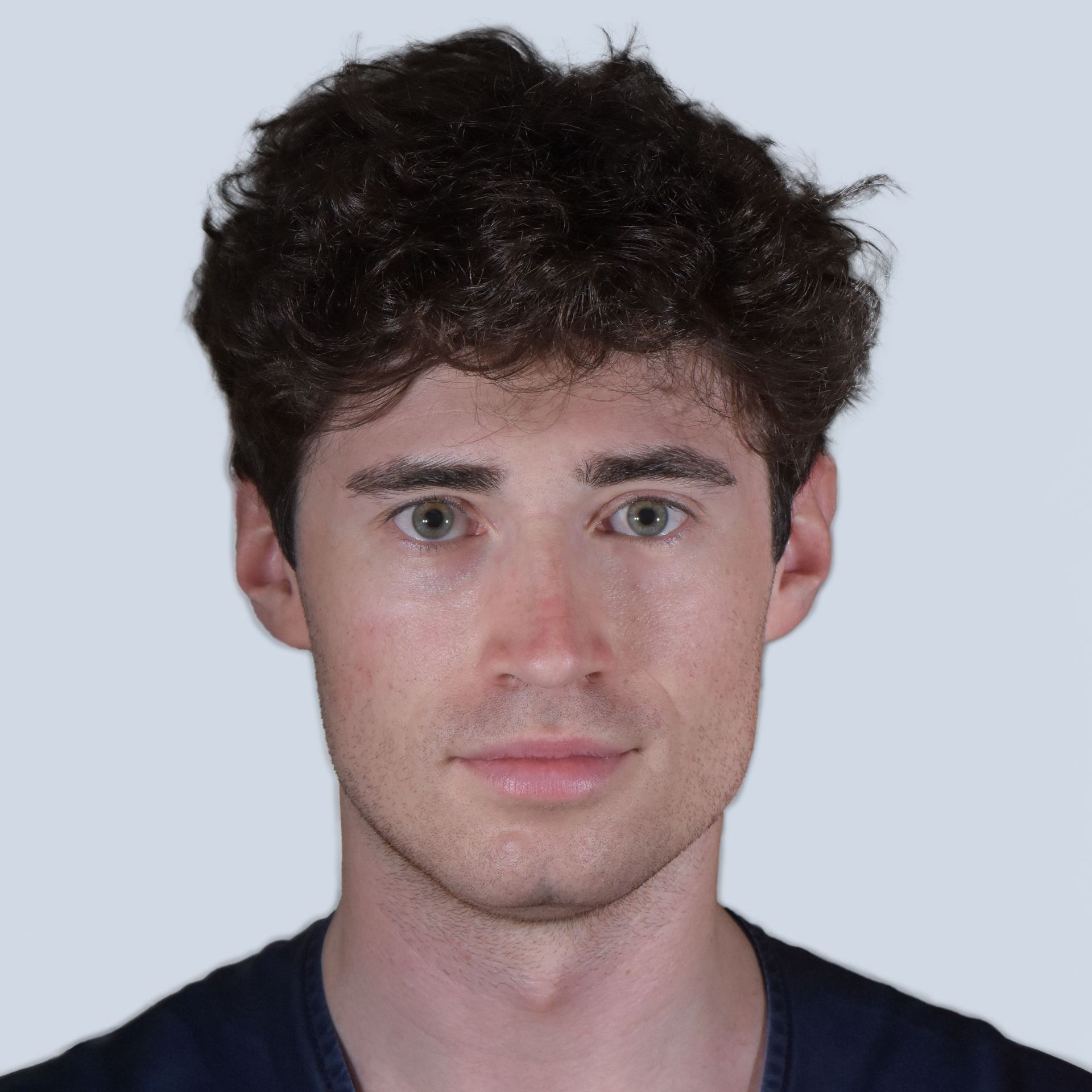 Un giovane uomo con la pelle chiara, i capelli castani ricci e gli occhi grigio-azzurri, che guarda direttamente l'osservatore.