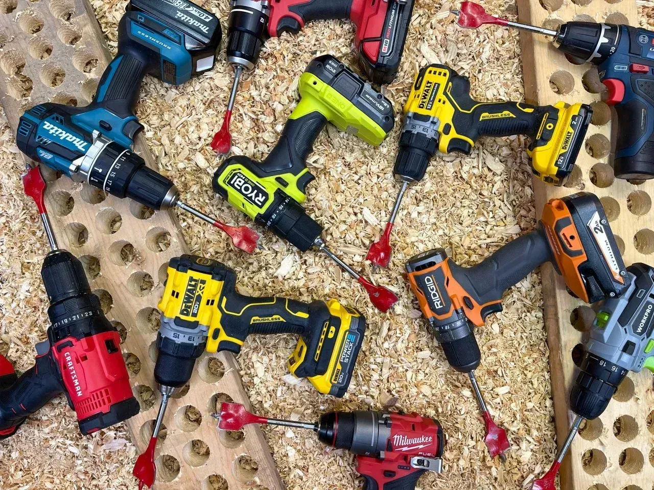 Drill drivers with auger attachments on wood shavings, varying colors and brands.