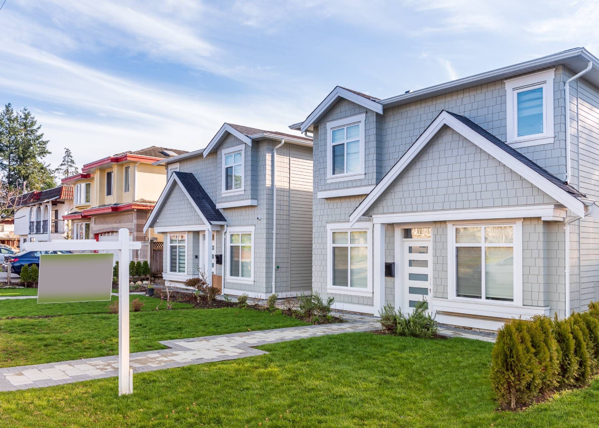 Row of modern houses with manicured lawns and a for sale sign.