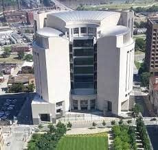 An aerial view of a modern, white courthouse building in a city, with a green lawn in front.