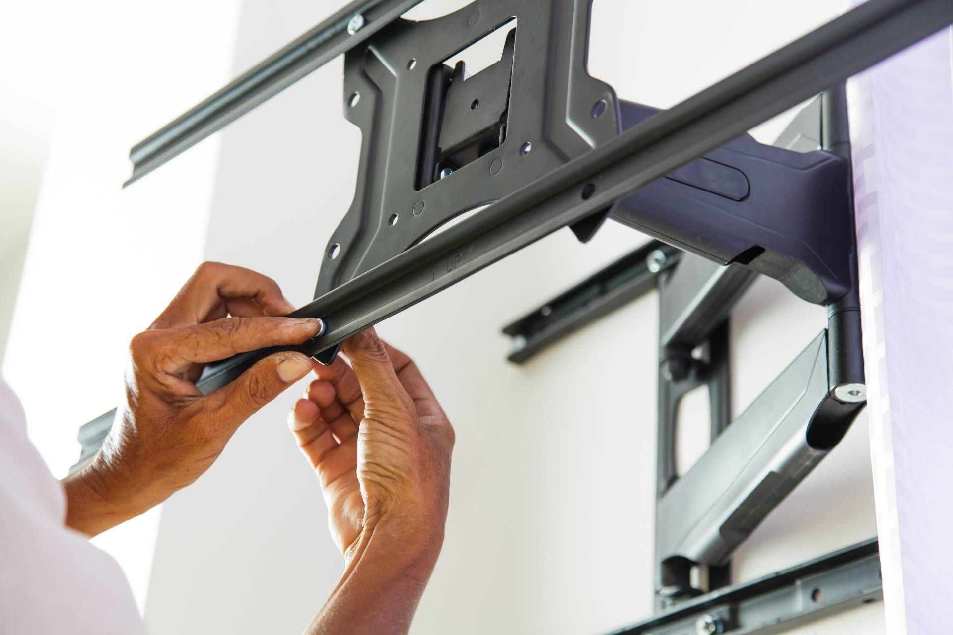 Person installing a black TV mount on a white wall, adjusting a sliding bar.