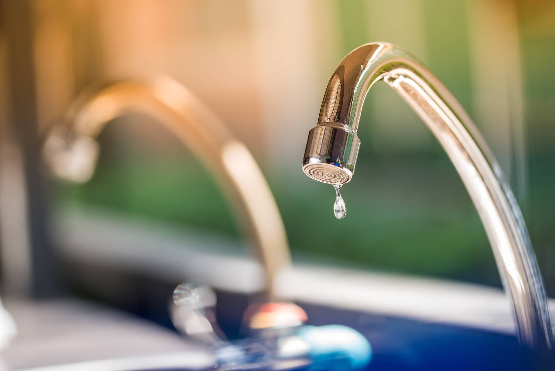 Close-up of a chrome faucet with a single water drop falling.