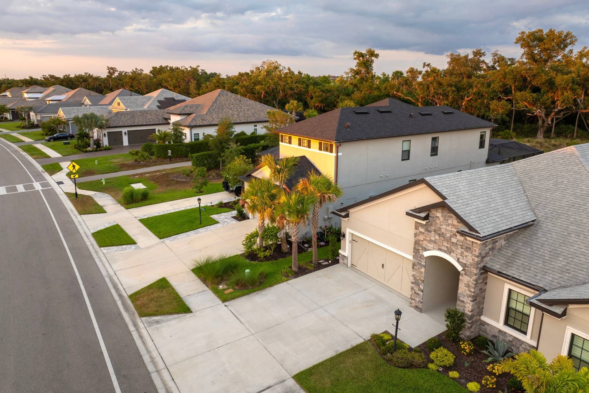 Suburban homes along a road at dusk. Light-colored houses with driveways and landscaping.