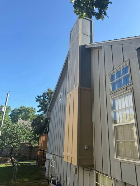 Side view of a two-story house with light siding, a chimney, and windows against a blue sky.