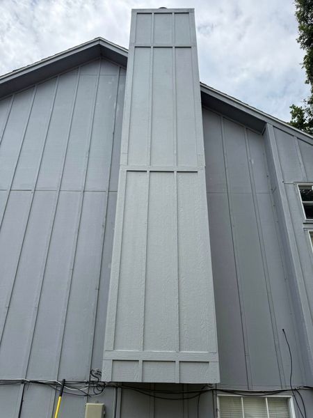 Gray chimney on the side of a gray house, with visible seams and a cloudy sky.