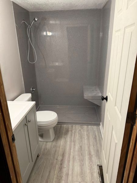 Gray bathroom with walk-in shower, toilet, vanity, light wood-look flooring.