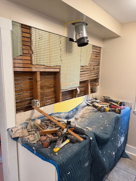 Renovation in progress: wall with exposed studs, tools, dust, covered countertop, vent.