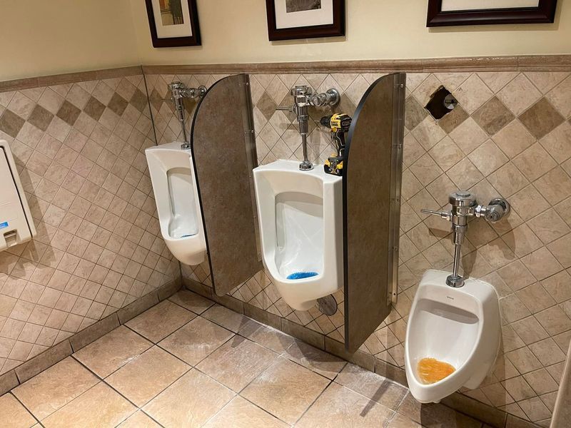 Public restroom with three urinals, beige tile walls and floor, and wooden privacy dividers.