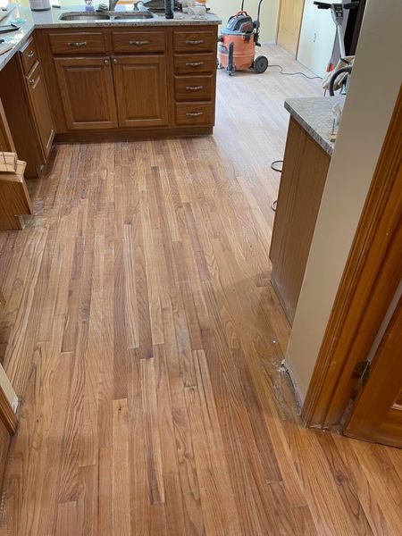 Wooden kitchen floor with brown cabinets being installed.