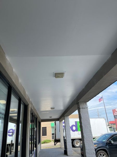 White building awning with pillars; FedEx truck and flag in the background.