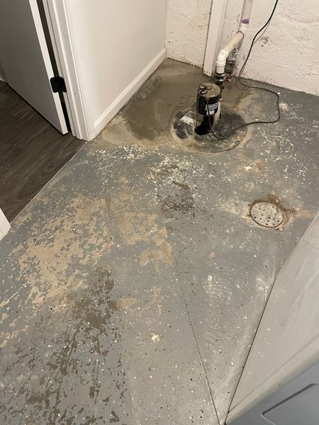 Gray basement floor with sump pump, wet spots, and peeling paint.