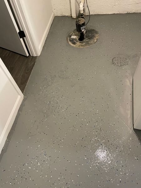 Gray epoxy floor with white speckles, a sump pump, and a drain in a basement.