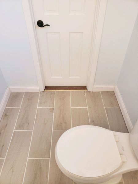 A toilet in a small bathroom with light wood-look floor tiles and a white door.