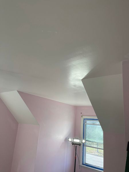 Pink-painted room with angled ceiling and window. Light reflects on the ceiling and walls.