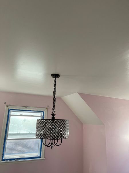 A pink-walled room with a chandelier hanging from a white ceiling, next to a window.