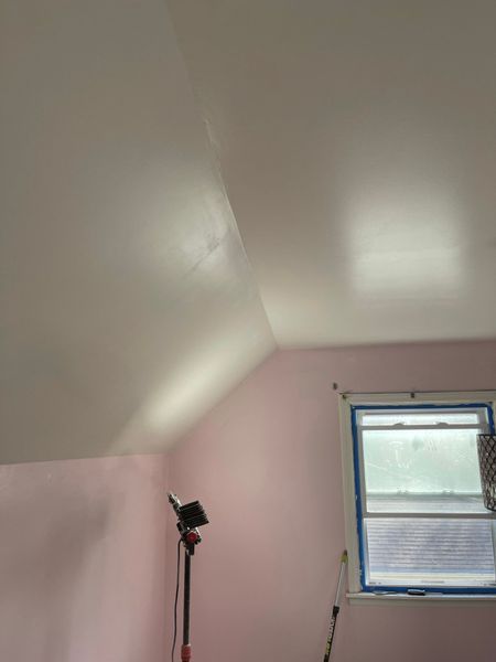 Pink-walled room with white sloped ceiling; a window with blue tape; a light stand in the corner.