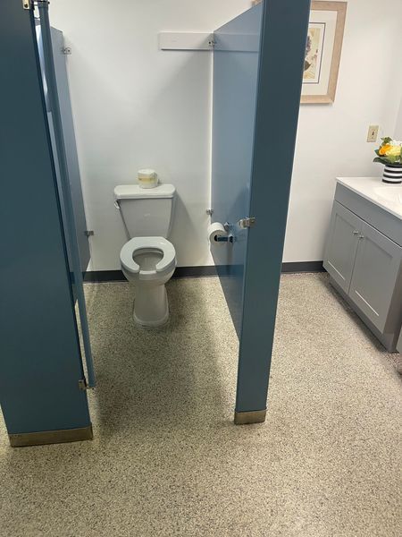Public restroom with blue stall doors, white toilet, and speckled flooring.
