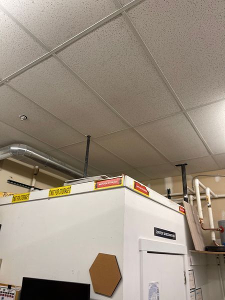 White ceiling tiles with metal supports over a white machine in a lab.