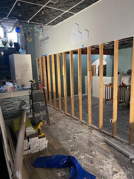 Construction site: wooden wall framing, exposed studs, tools, debris, and person working.