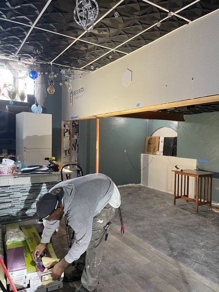 Man working on construction project in room. Gray walls, dark ceiling, wood floors, and some completed sections.