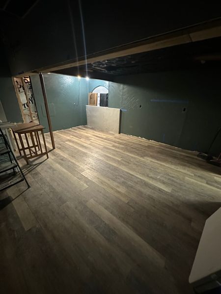 Basement room with wood-look floor, green walls, and a small wooden table.