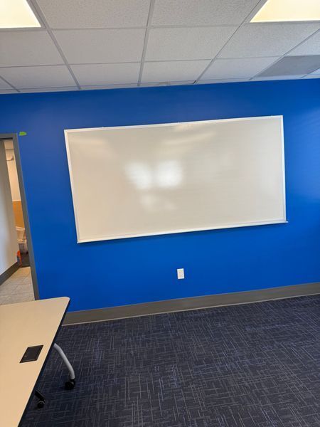 Blue classroom wall with a whiteboard, an electrical outlet, and a table.