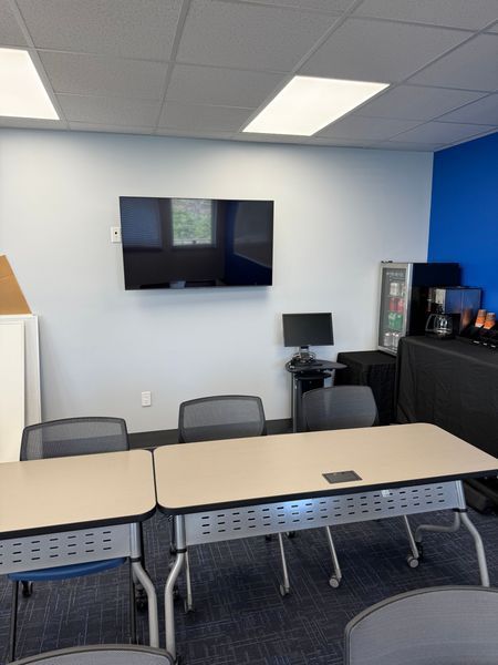 A training room with tables, chairs, a large TV, computer, and coffee station. Blue and white walls.