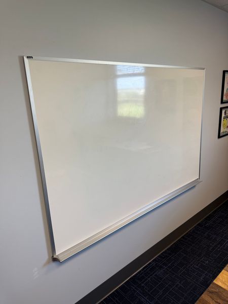 Whiteboard mounted on a gray wall with a silver frame and a small shelf at the bottom.