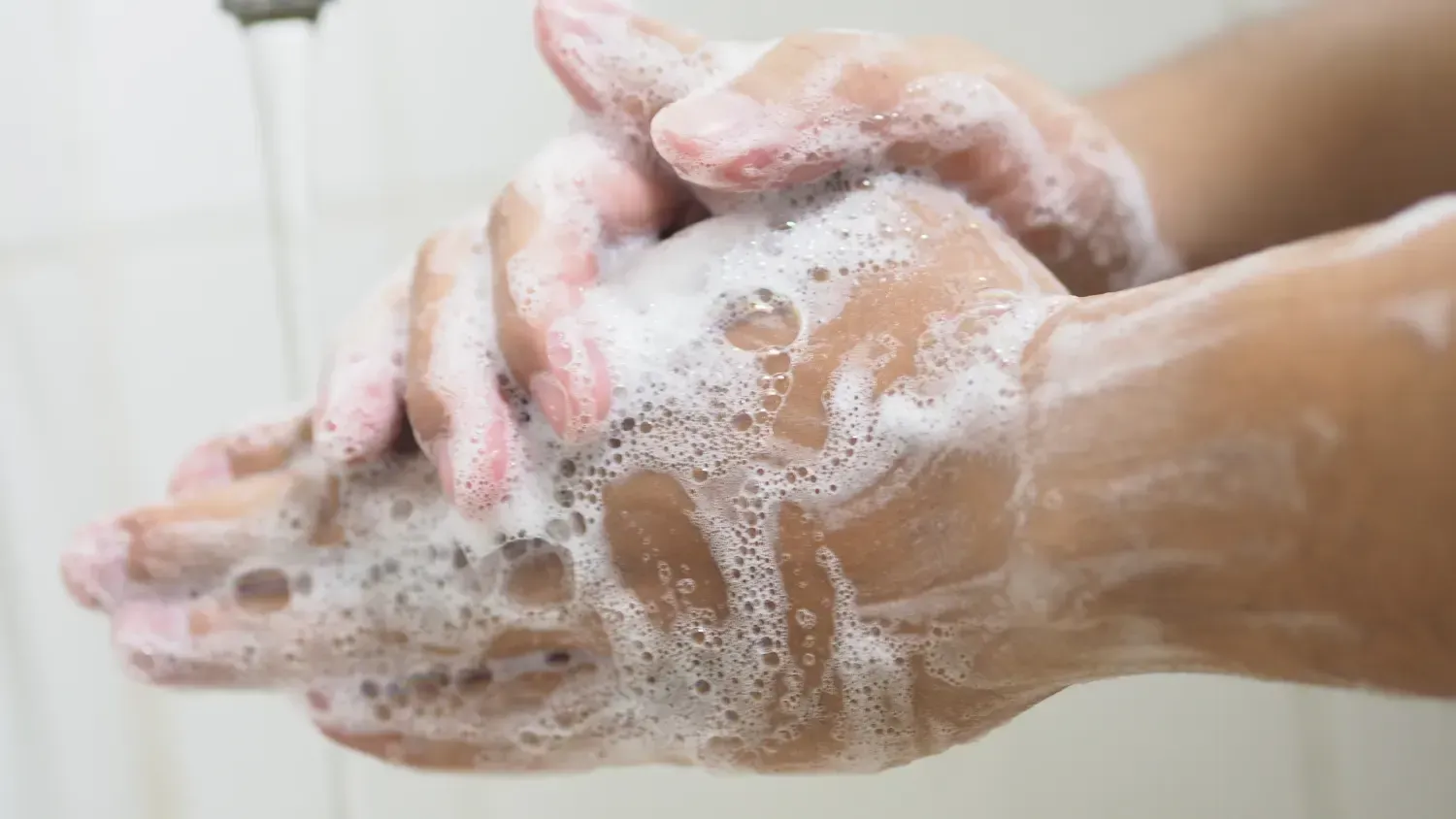 Hands covered in white soapy foam, washing under a faucet.