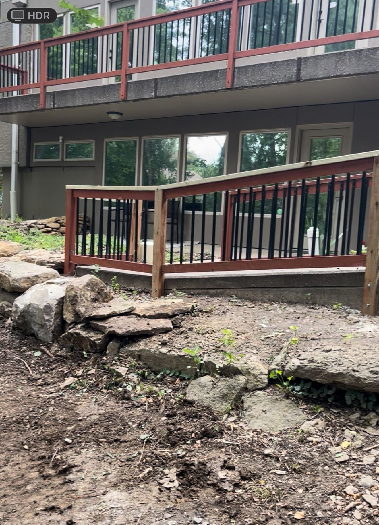 A home's lower level deck with a wooden railing, and rock landscaping in the yard.
