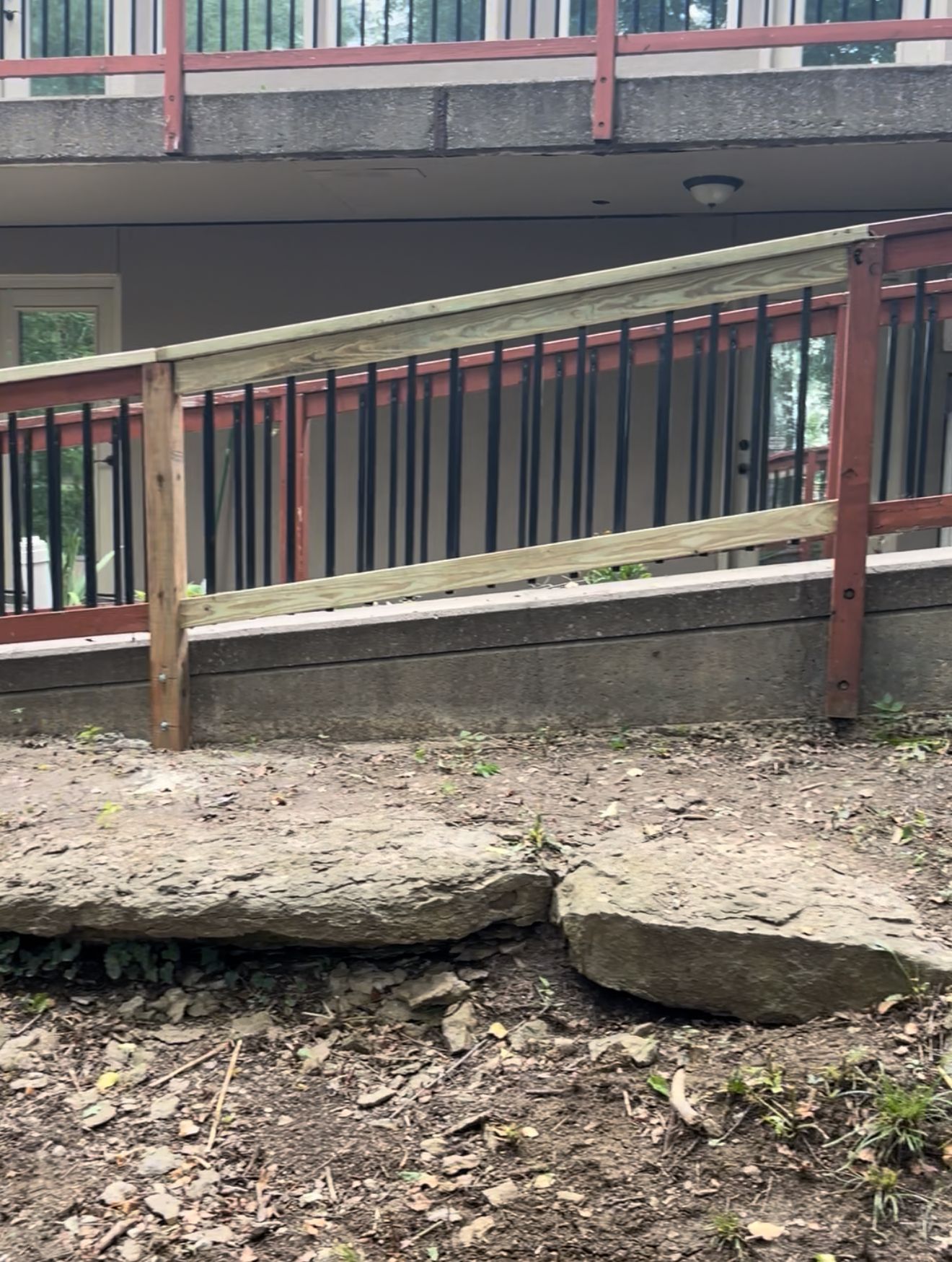 Ramp with wooden railings and black spindles. Concrete base with two broken stone steps.