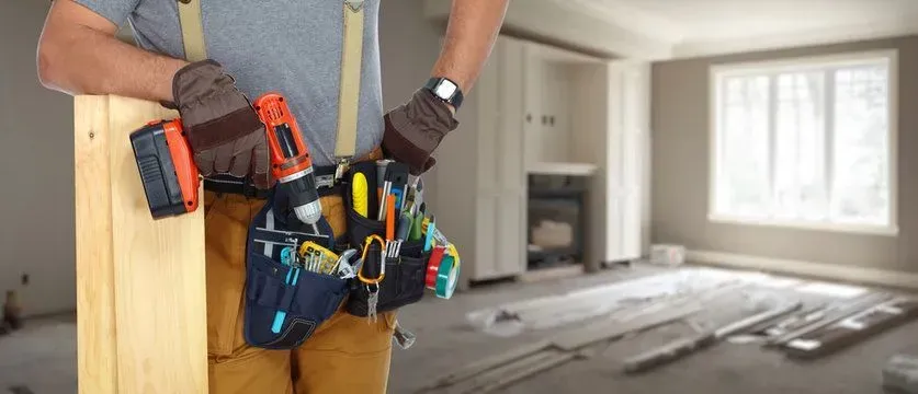 Construction worker with tool belt and drill, in a room under renovation.