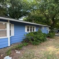 Blue house with white trim and lush green trees in the background.
