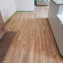 Hardwood floors, light-colored, with a view of the corner and a part of a brick wall.