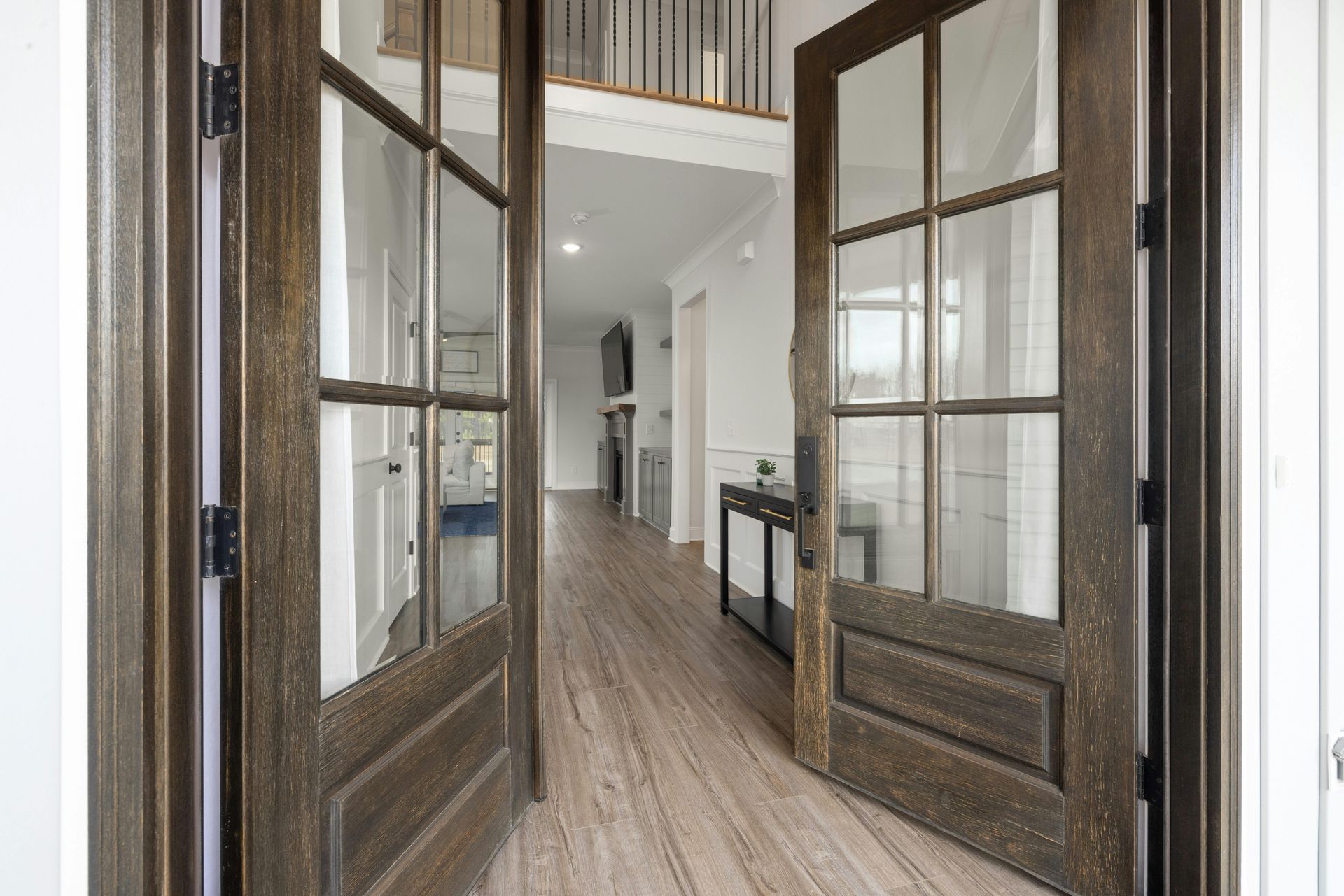 Open French doors to a bright hallway with wood floors and black-framed windows