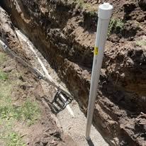 Trench with white pipe and buried pipes, in dirt and grass.