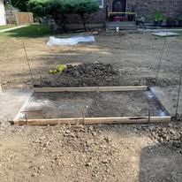 A concrete slab under construction with wooden forms, surrounded by dirt and debris outdoors.