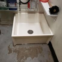 A white utility sink with a drain in a light, cement-floored room.