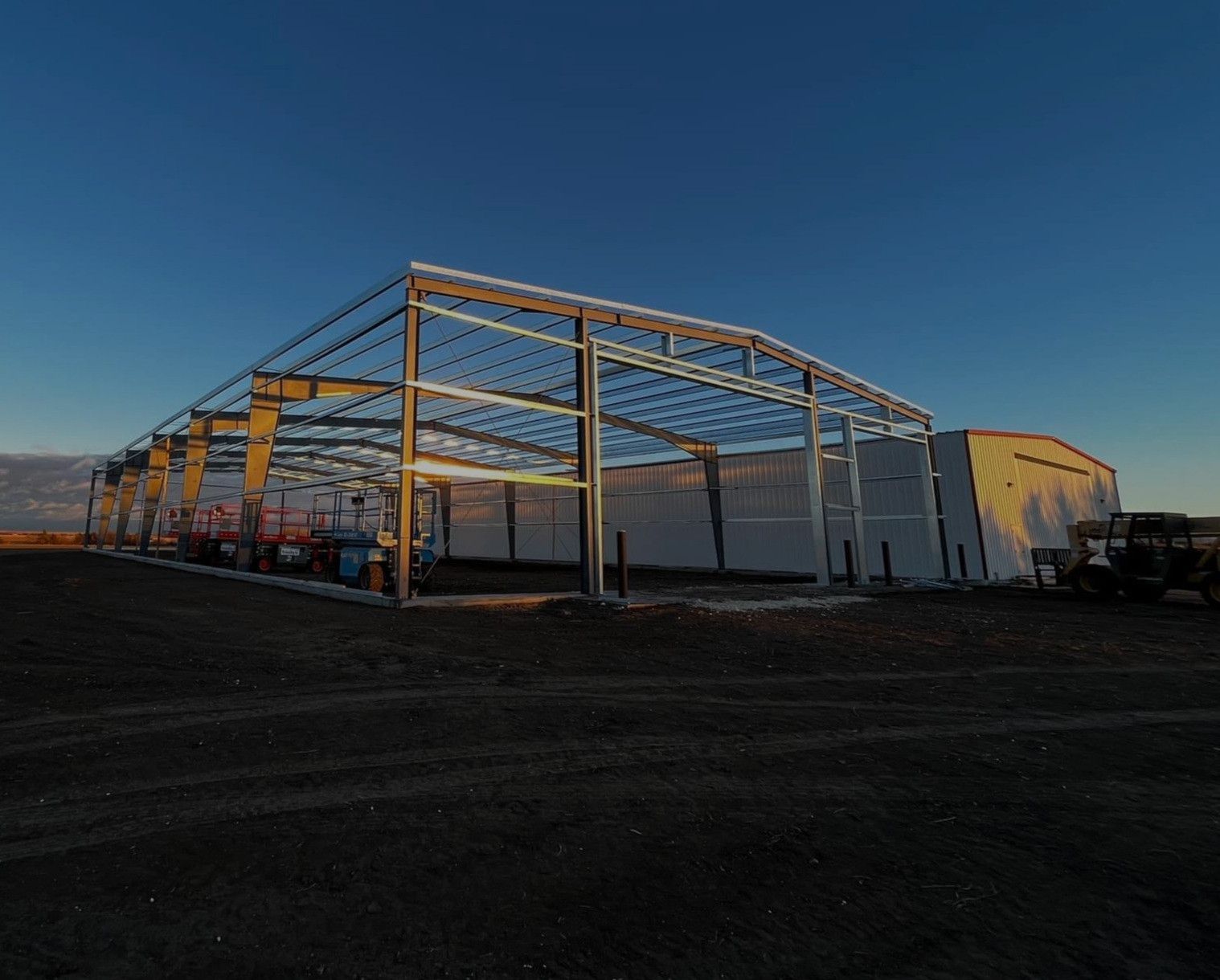 Steel frame of a large building under construction in a field against a blue sky.