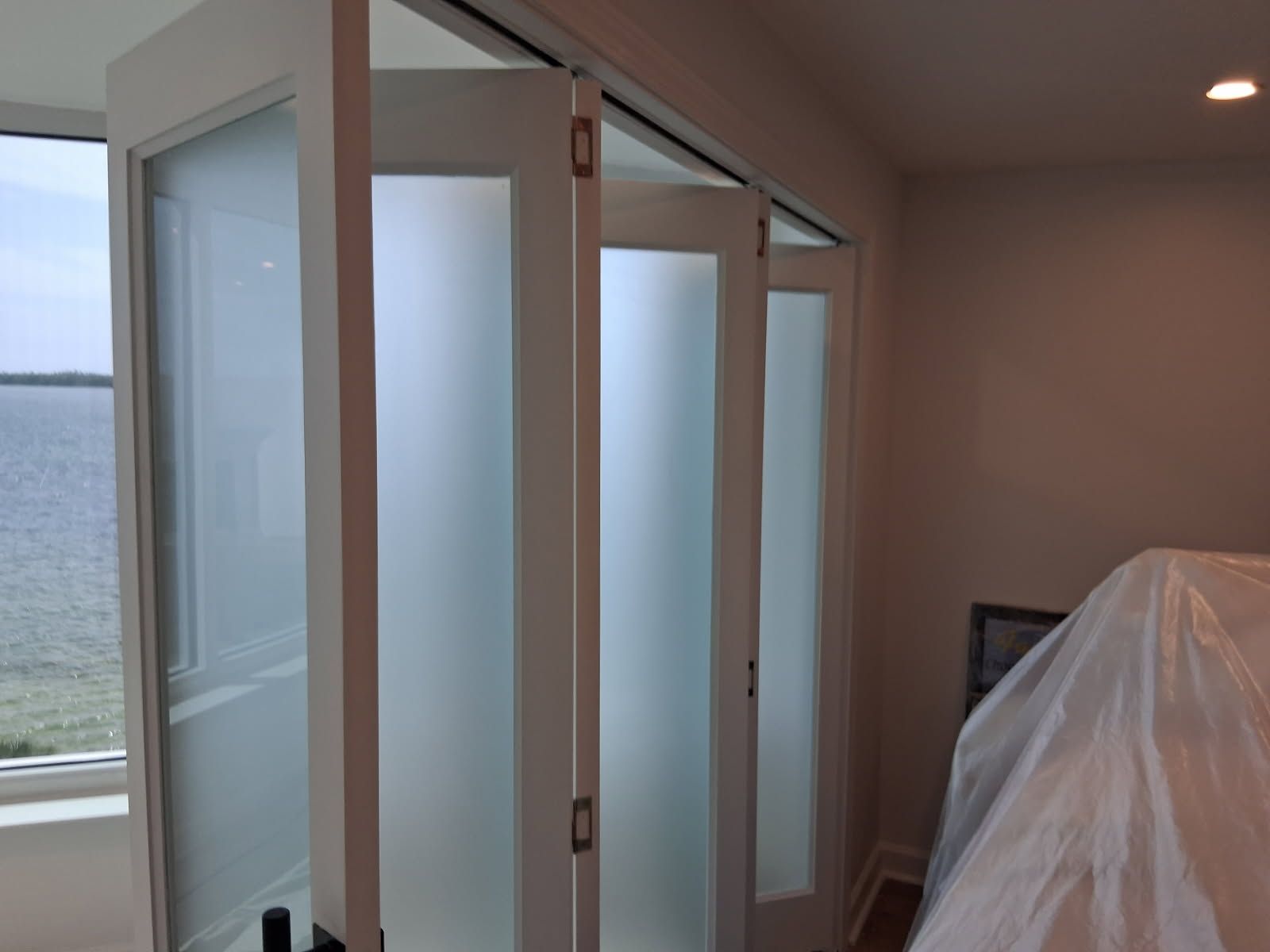 White folding doors with frosted glass, partially open in a room with a water view.