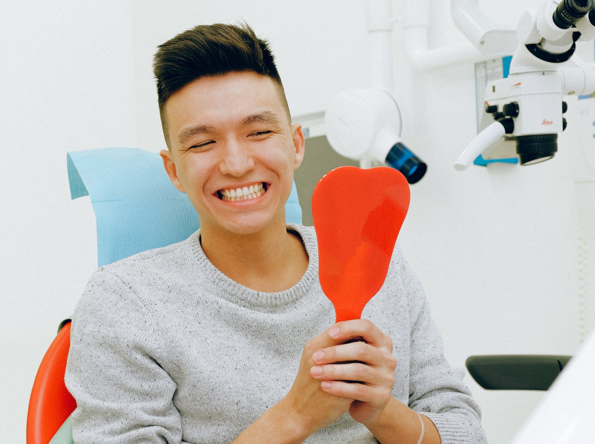 A man is sitting in a dental chair looking at his teeth in a mirror.